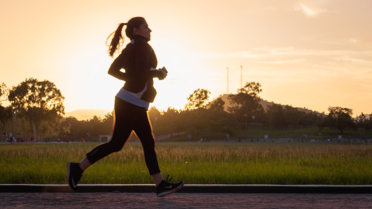 Mulher correndo ao pôr do sol questionando se corrida emagrece de verdade